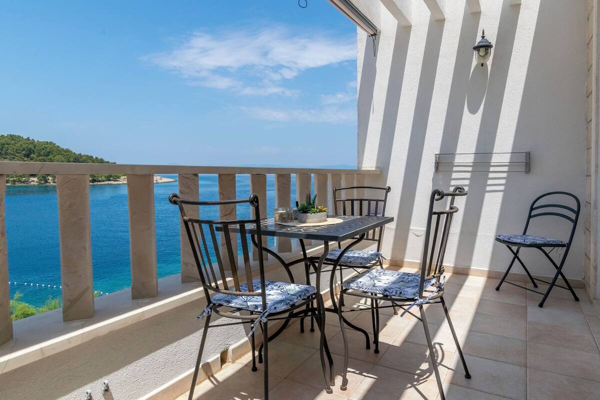 A balcony with a table and chairs, overlooking a body of water and a distant shoreline.