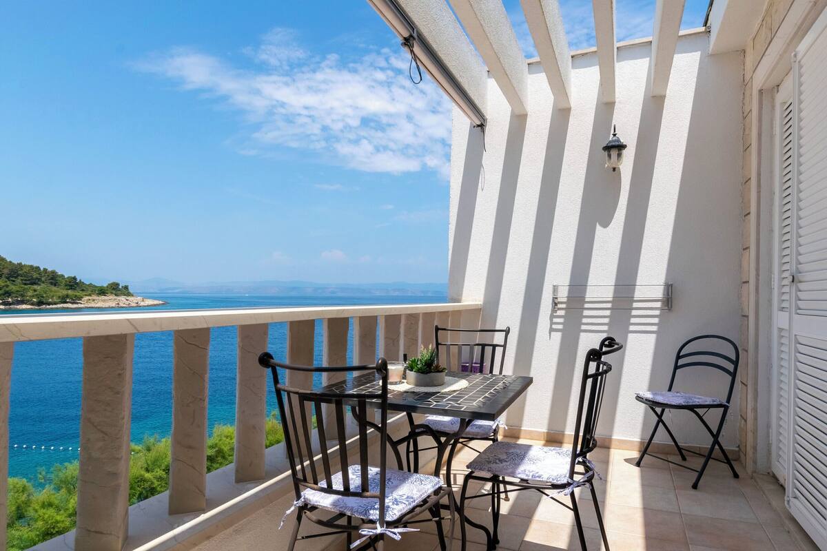 A balcony with a table and chairs, overlooking a coastal view.
