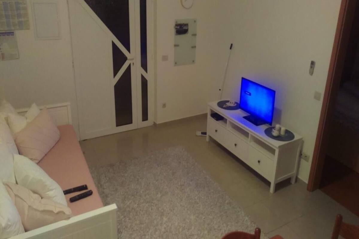 Un salon comprenant un canapé, un téléviseur posé sur un meuble, une armoire blanche et une porte donnant sur une autre pièce.