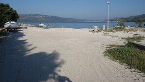 Una playa arenosa con barcos, un farol y una vista despejada del agua y las colinas al fondo.