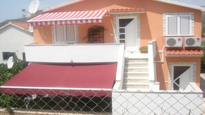 Una casa de dos pisos con un toldo rojo, contraventanas blancas y antenas parabólicas.