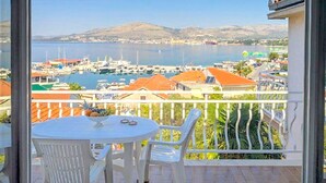 Uma varanda com mesa e cadeiras, com vista para uma marina com barcos e uma montanha ao longe.