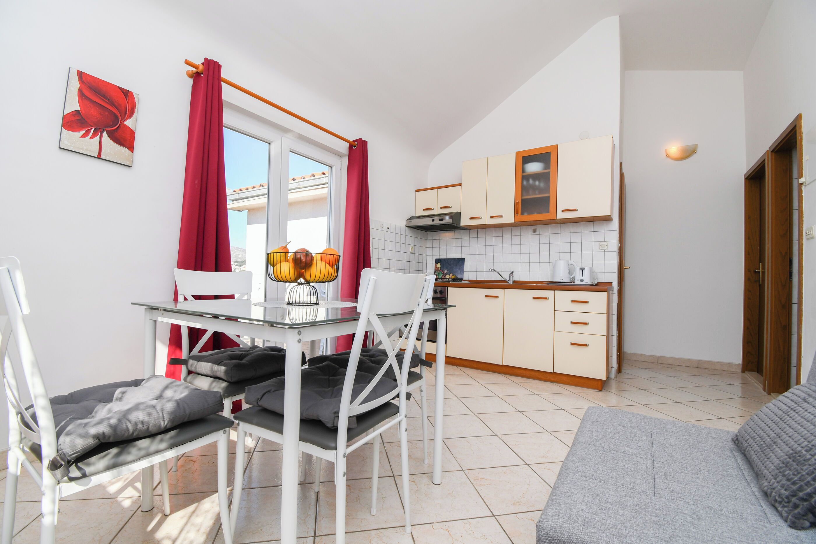 Una cucina compatta con zona pranzo, che include un tavolo con sedie, un divano e una finestra con tende rosse.