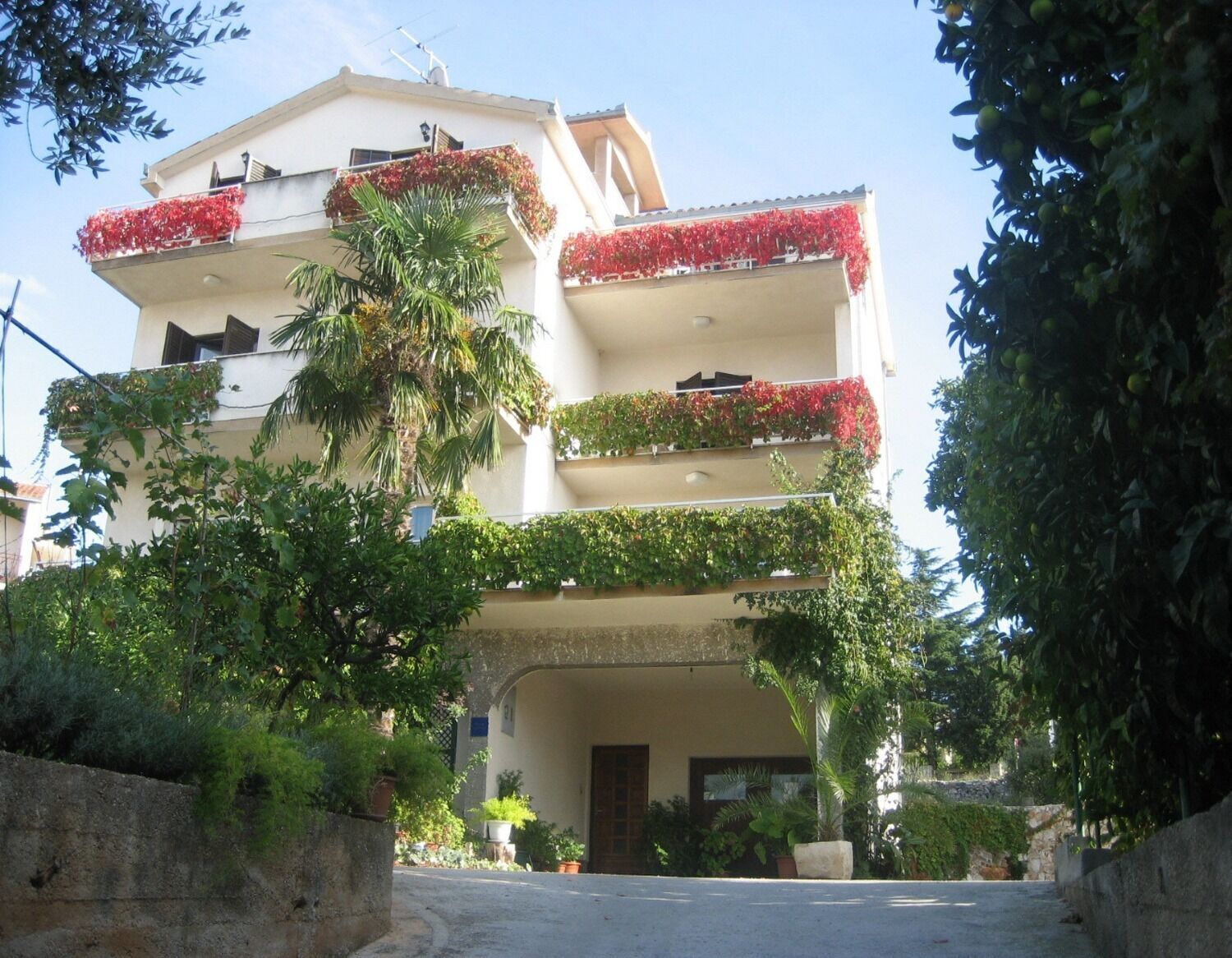 A multi-story building with balconies adorned with red flowers and green foliage.