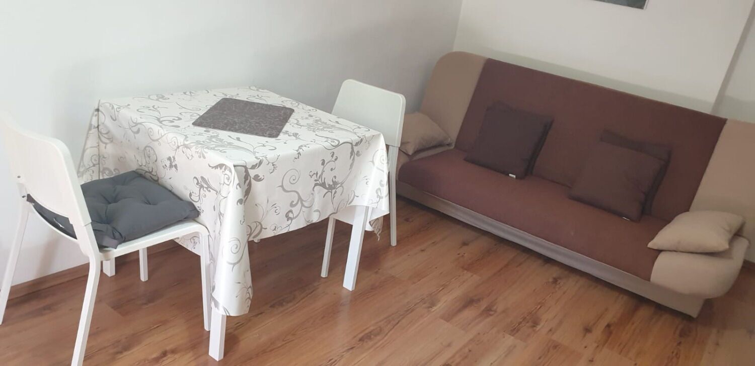 Un coin repas avec une table recouverte d’une nappe à motifs, un canapé marron avec des coussins et des chaises blanches.