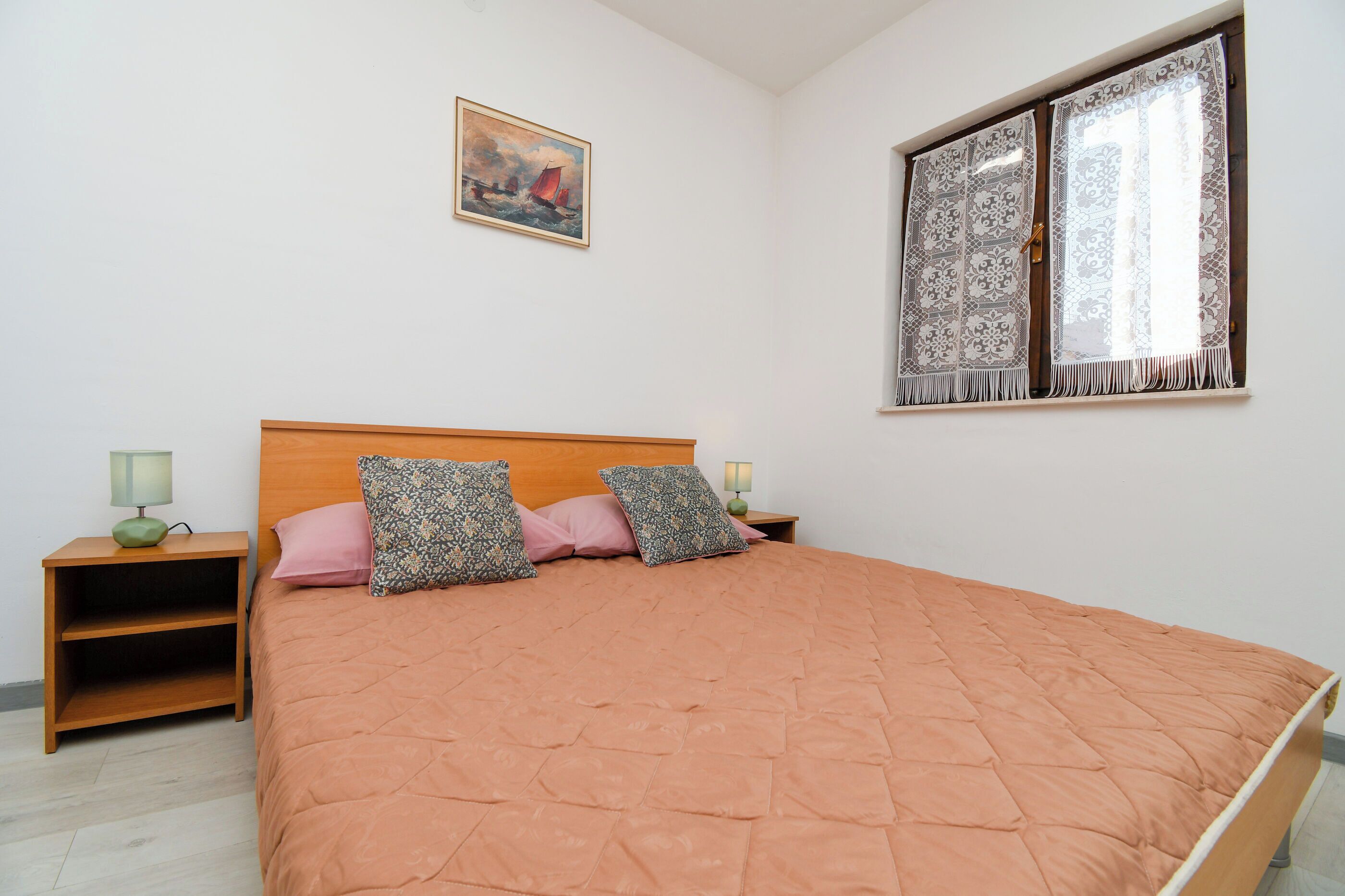 A bedroom with a wooden bed, two nightstands, a painting, and a window with patterned curtains.