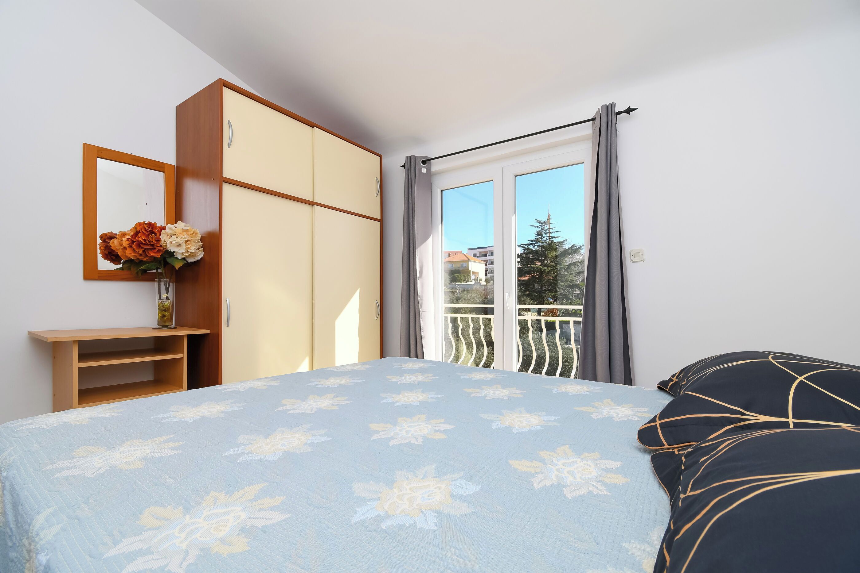 Une chambre à coucher avec un lit, une armoire, un miroir et une fenêtre avec des rideaux.