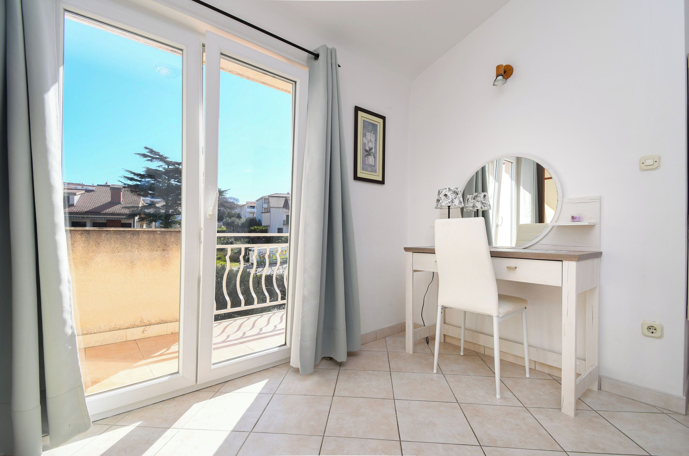 A room with a desk, chair, and a large window with a view of buildings and trees.