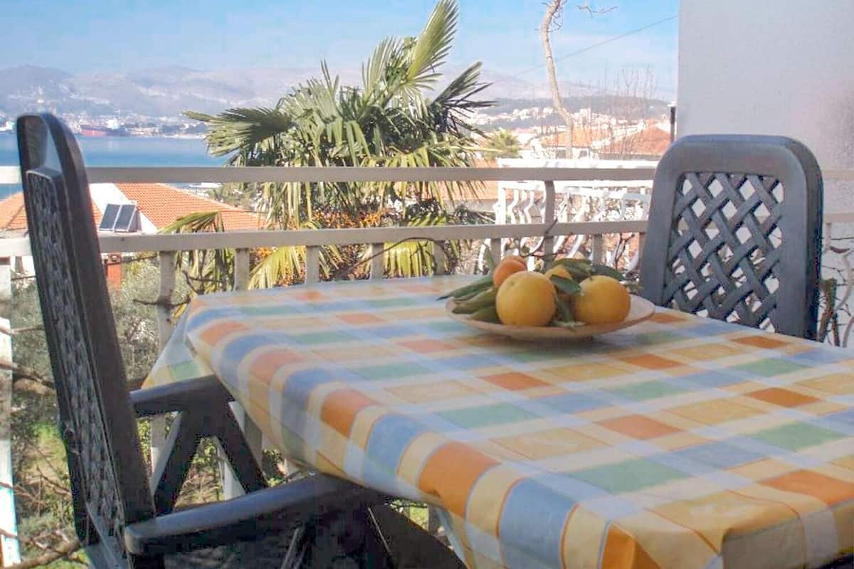 A balcony with a table set for two, a view of the sea, and a palm tree.