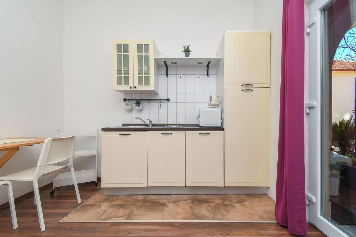 A compact kitchen with white cabinets, a small countertop, and a window with a view of the outside.
