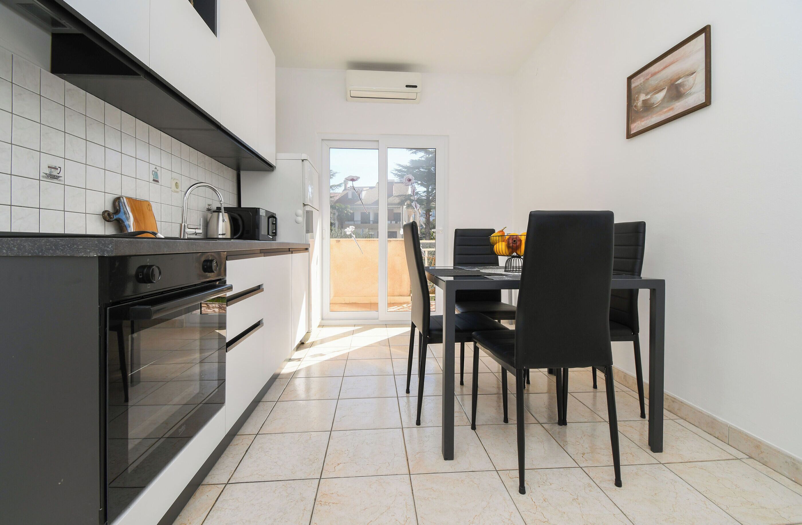 A modern kitchen with a dining area, featuring a black countertop, white tiled backsplash, and a dining table with chairs.