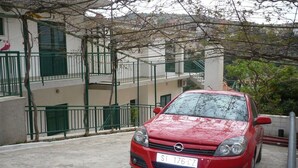 A red car parked in a covered parking area with a building in the background. - Apartments Neva (Primosten)