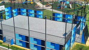 A multi-story building with a sports court, surrounded by a fence and greenery. - Apartments Neva (Primosten)