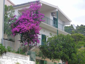 A building with a balcony, a staircase, and a tree with purple flowers. - Apartments Neva (Primosten)