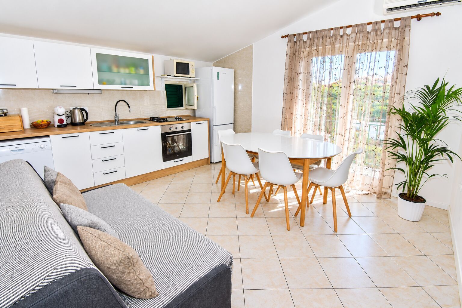 A modern kitchen with white cabinets, a dining area with a white table and chairs, and a large potted plant.