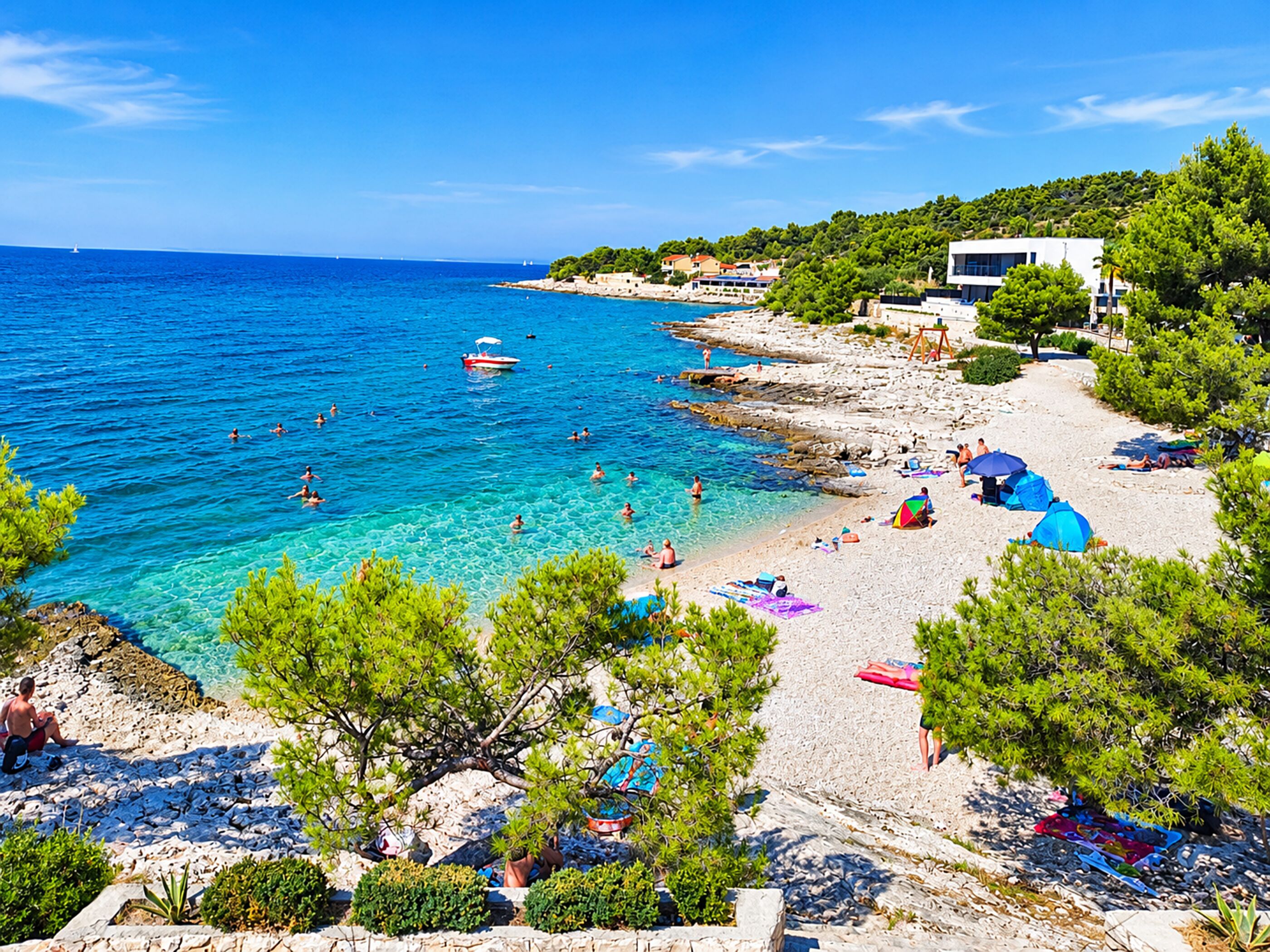 A coastal beach with clear waters, rocky shoreline, and a few buildings in the background.