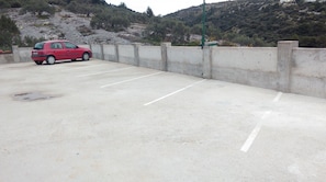 A parking area with a red car parked in one of the spaces. - Apartments Neva (Primosten)