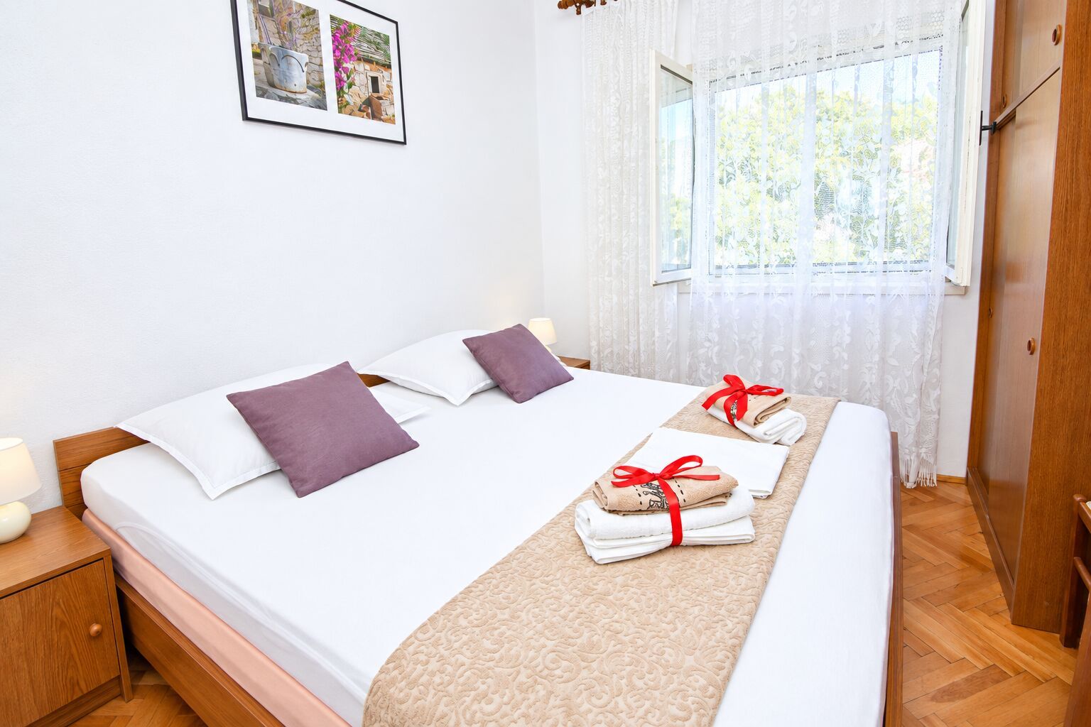 A neatly made bed with pillows, a bedside table with a lamp, and a window with curtains.