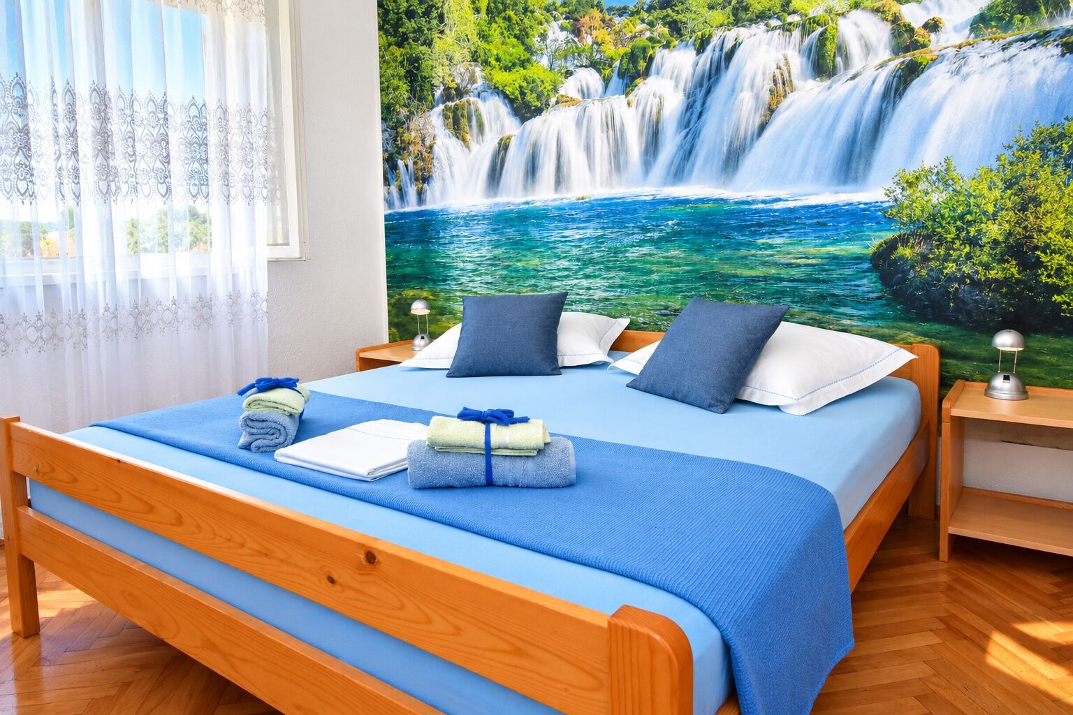 Ein Hotelzimmer mit einem großen Bett, einem Nachttisch, einer Lampe und einem Wandbild eines Wasserfalls.