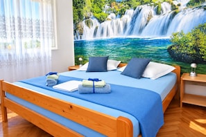A hotel room with a large bed, a nightstand, a lamp, and a mural of a waterfall. - Apartments Neva (Primosten)