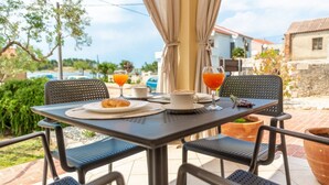 Un área de comedor al aire libre con una mesa preparada para dos, que incluye un croissant y una taza de café.