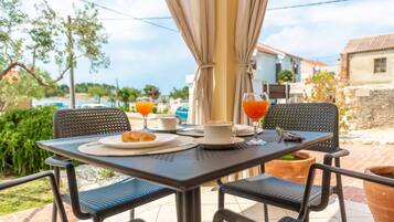 An outdoor dining area with a table set for two, featuring a croissant and a cup of coffee.