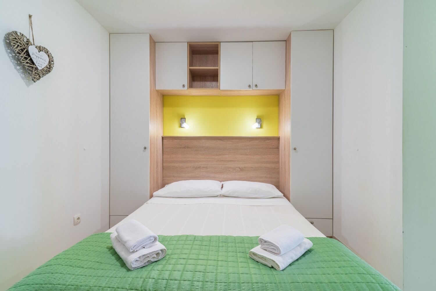 Habitació compacta amb un llit, dos mobles penjats a la paret i una petita prestatgeria.