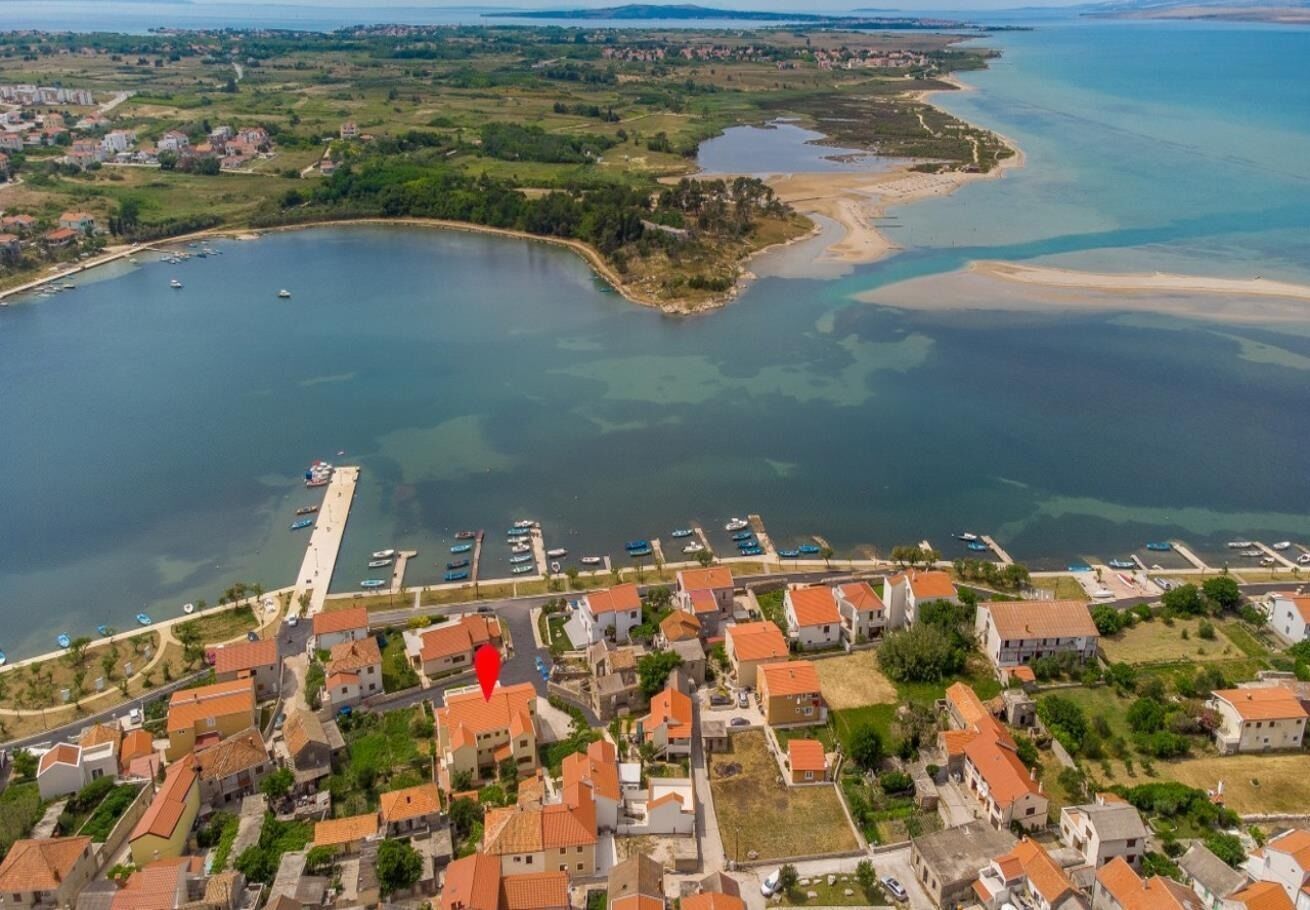 Vista aérea de un pueblo costero con un puerto deportivo, edificios residenciales y un muelle que se adentra en el agua.