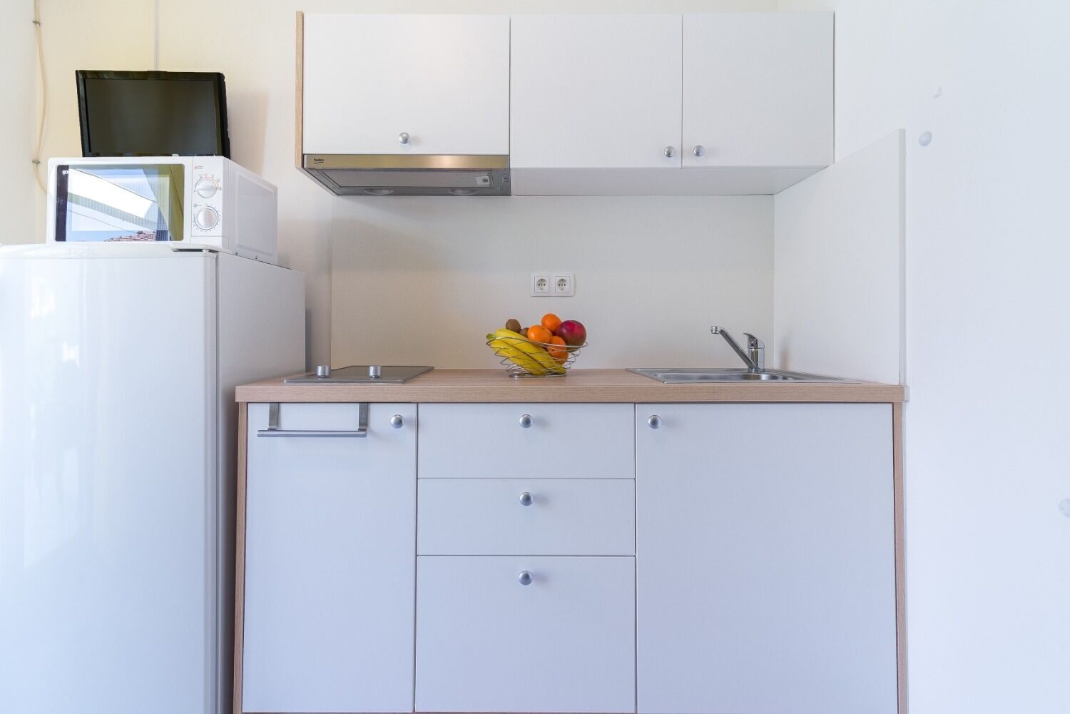 A compact kitchen with white cabinets, a microwave, a sink, and a fruit bowl on the countertop.
