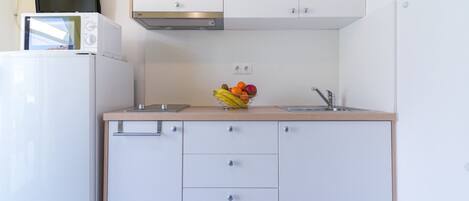 A compact kitchen with white cabinets, a microwave, a sink, and a fruit bowl on the countertop.