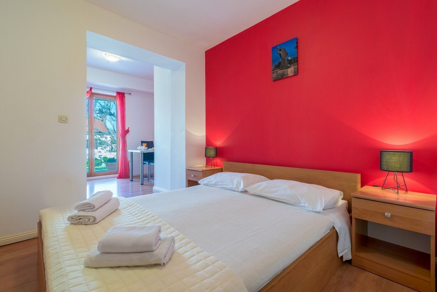 Habitació d'hotel amb un llit gran, una taula de treball i una paret vermella decorativa.