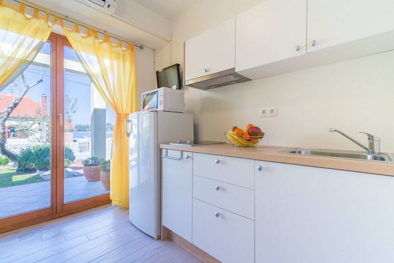 Una cucina compatta con frigorifero, forno a microonde e una ciotola di frutta sul piano di lavoro.