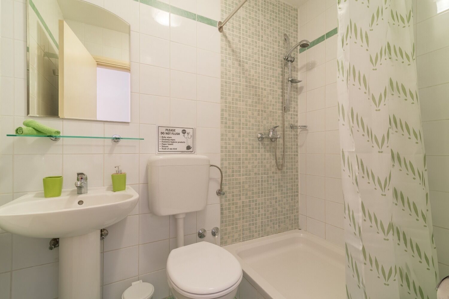 Ein Badezimmer mit Toilette, Waschbecken und Dusche. Ein Schild an der Wand bittet darum, keine Papierhandtücher herunterzuspülen.