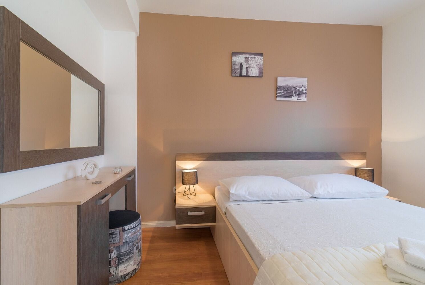 A hotel room with a bed, bedside tables, a mirror, and two wall-mounted pictures.