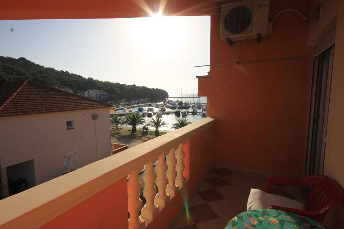 A balcony with a view of a marina and boats, a red chair, and a patterned tablecloth.