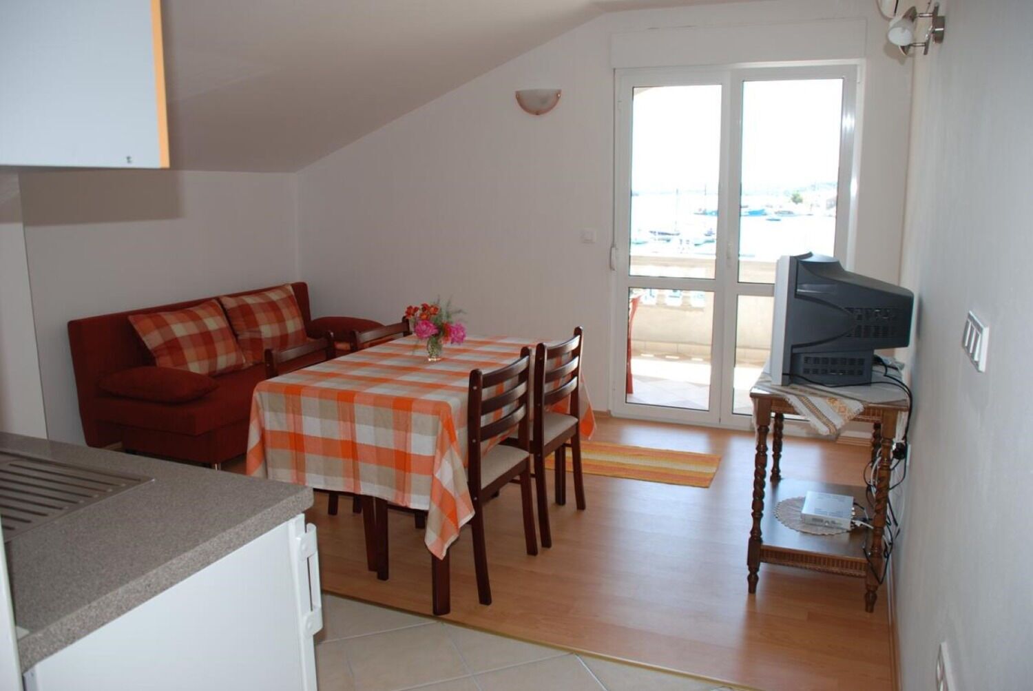 Un espacio habitable compacto con una mesa de comedor, sillas, un sofá, un televisor y un ventanal corredero que da a un área exterior.