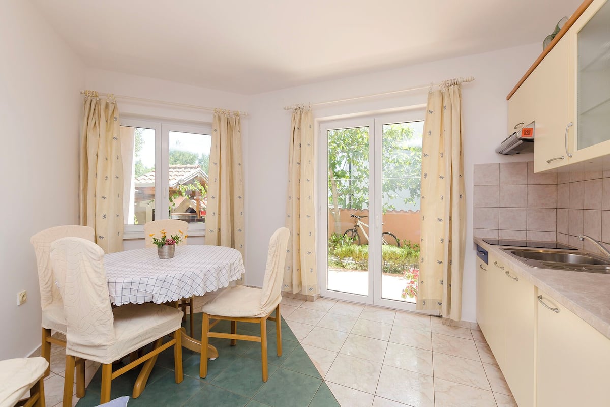A dining area with a table and chairs, a kitchen with a sink, and a sliding glass door to the outside.