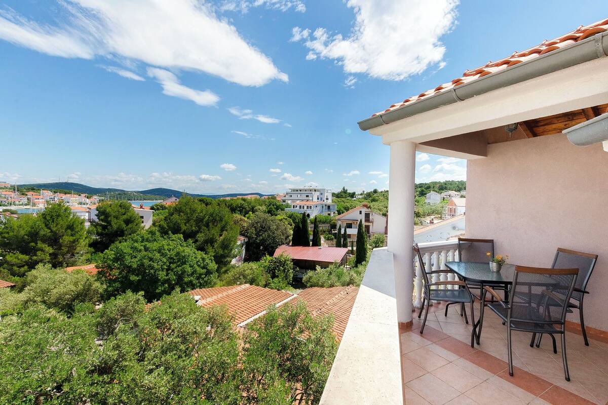 A balcony with a table and chairs, overlooking a residential area with houses and trees.