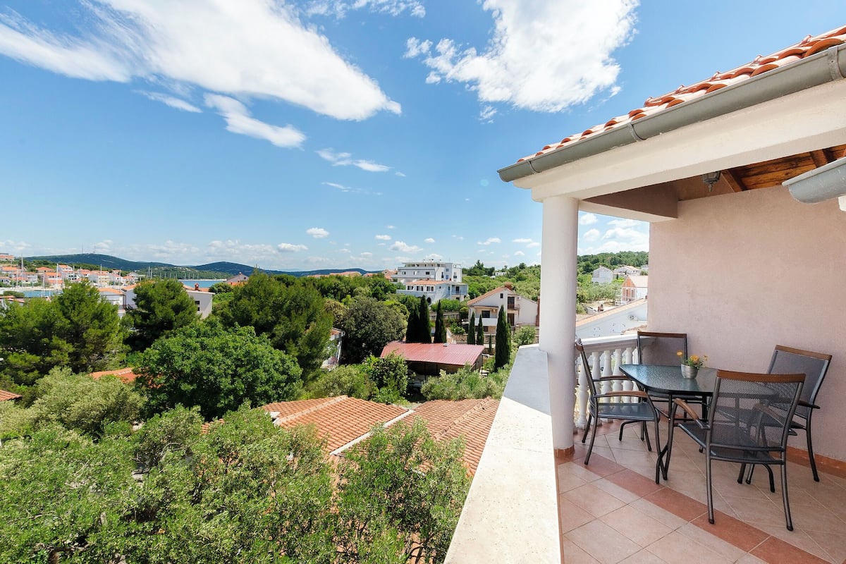 A balcony with a table and chairs, overlooking a residential area with houses and trees.