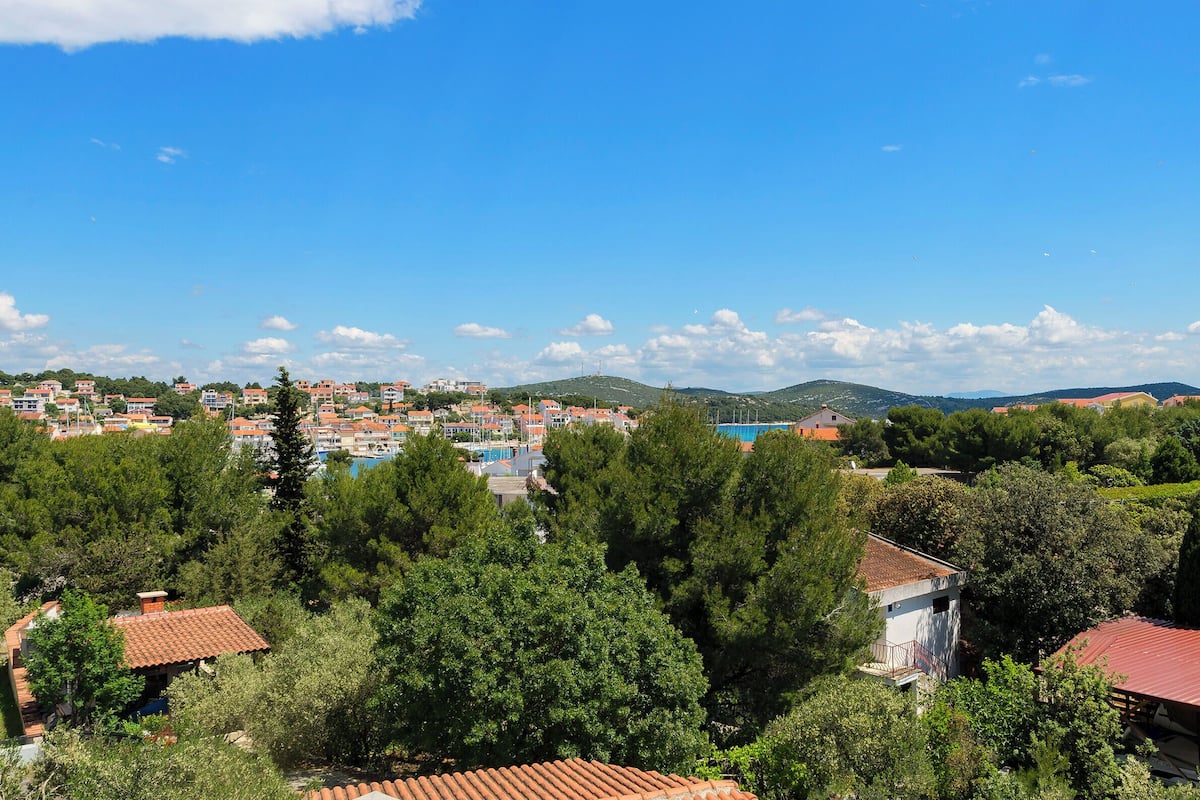 A coastal town with buildings, a swimming pool, and dense greenery.