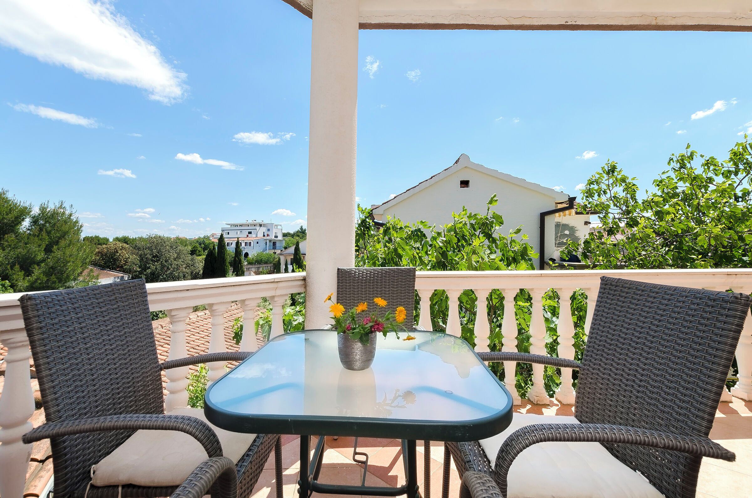 A balcony with wicker chairs, a glass table, and a vase of flowers.