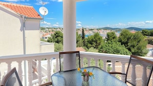 A balcony with a table and chairs, a satellite dish, and a view of a town and hills. - Apartments Dragan (Tisno)