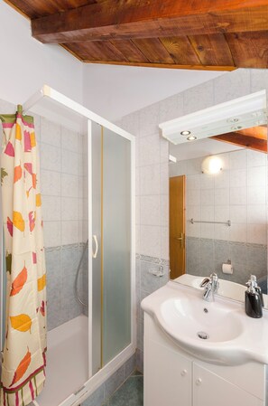 A bathroom with a shower, a sink, a mirror, and a wooden ceiling. - Apartments Dragan (Tisno)