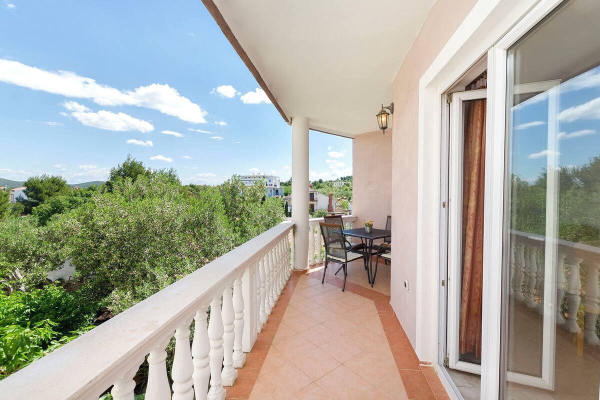 A balcony with a table and chairs, a white balustrade, and a view of greenery and buildings.