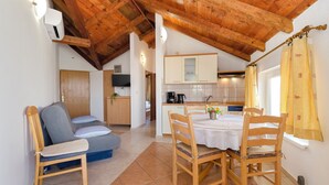 A cozy room with a wooden ceiling, a dining table with chairs, a sofa, and a kitchen area with cabinets and a coffee machine. - Apartments Dragan (Tisno)