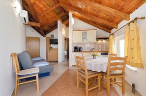 A cozy room with a wooden ceiling, a dining table with chairs, a sofa, and a kitchen area with cabinets and a coffee machine. - Apartments Dragan (Tisno)