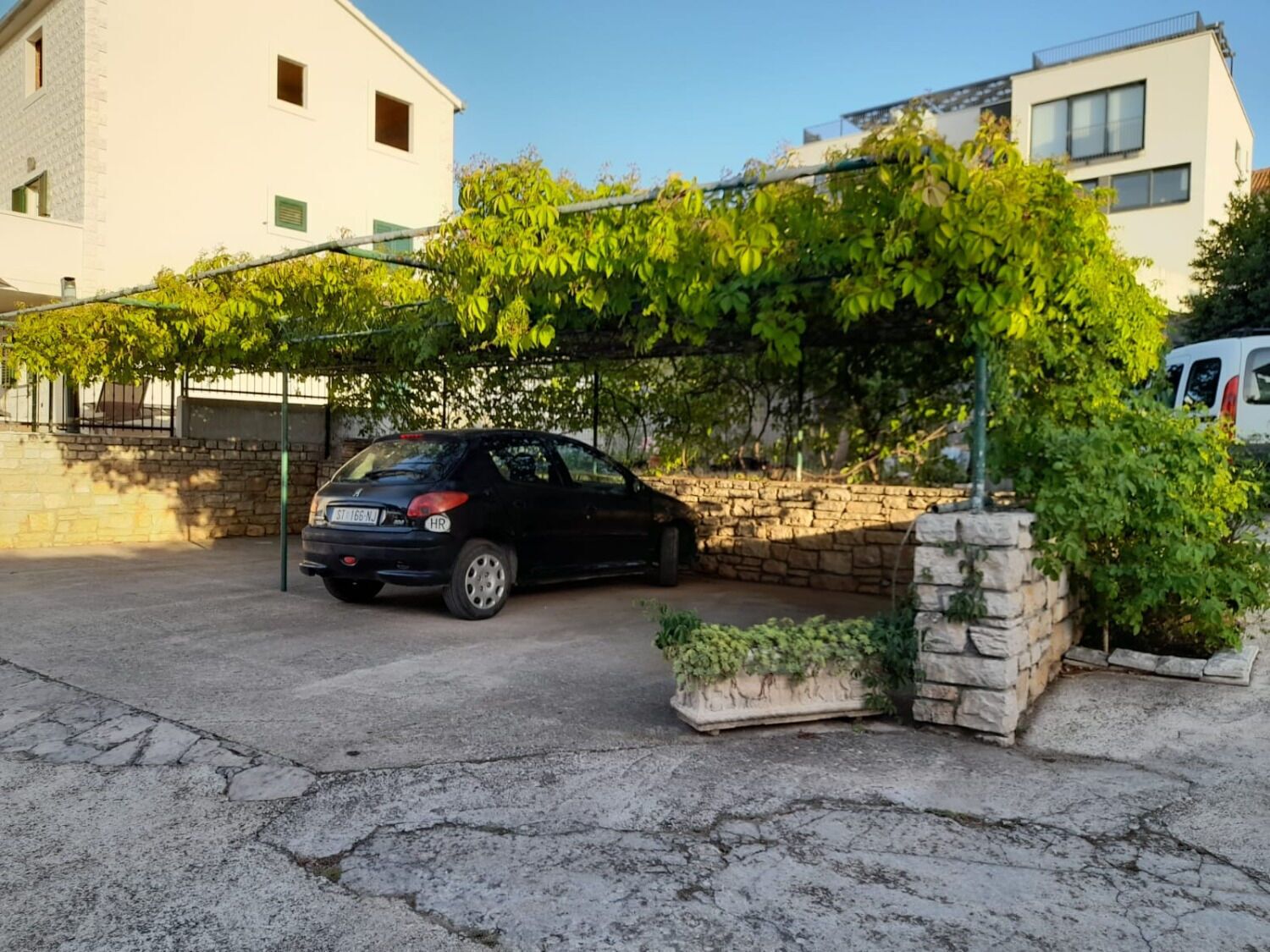 Une voiture noire est garée dans une allée bordée d’un mur de pierres, avec un bâtiment en arrière-plan.