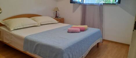 A neatly made bed with a blue bedspread and pillows, a bedside table with a lamp, and a window with curtains.