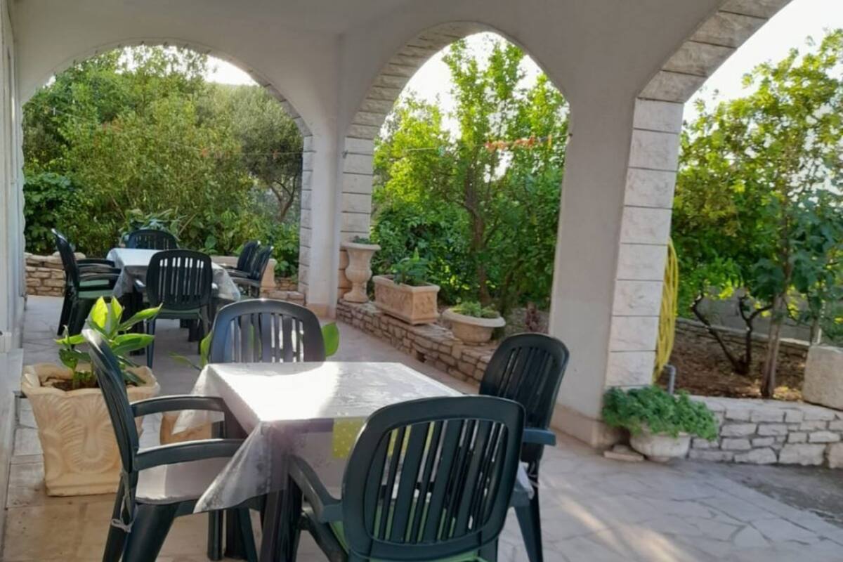 An outdoor patio with a stone table and chairs, surrounded by greenery and stone walls.