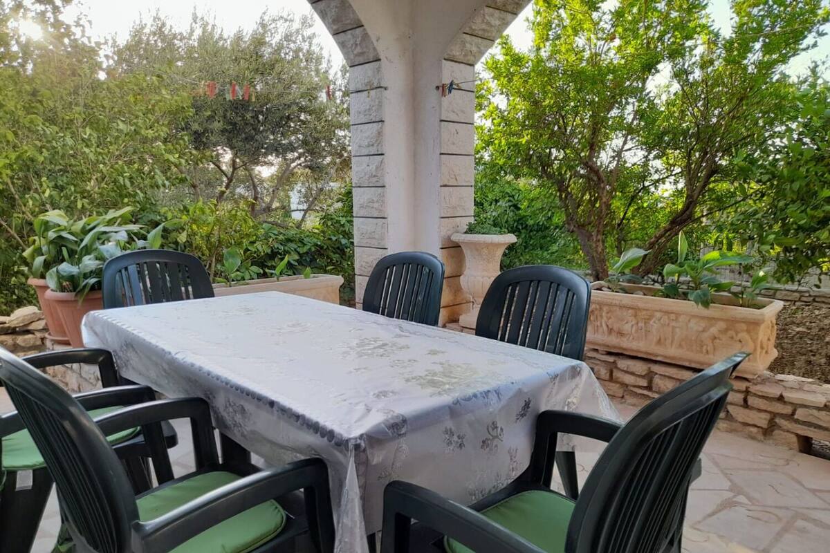An outdoor patio with a table and chairs, surrounded by greenery and stone walls.